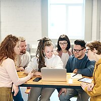 Eine Gruppe junger Menschen sitzt gemeinsam an einem Laptop und arbeitet.