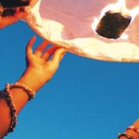 Hände halten einen kleinen selbst gebastelten Heißluftballon in den blauen Himmel.