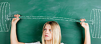 Ein Mädchen steht vor einer Tafel und hebt eine gezeichnete Hantel