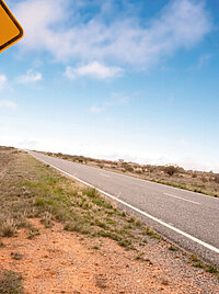 Eine Landstraße in Australien. Im Vordergrund steht ein gelbes Schild mit einem Känguru darauf.