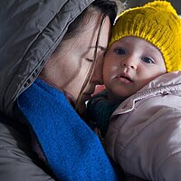 Eine Mutter hält ihr Kind im Arm und schließt die Augen. Beide tragen warme Kleidung. 