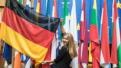 Eine Frau habt die Deutschlandfahne hoch. Im Hintergrund stehen weiter Flaggen. 