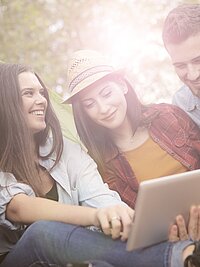Vier junge Menschen sitzen draußen im Grünen und schauen auf ein Tablet