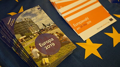 Zwei Informationsbroschüren liegen auf der Europaflagge.