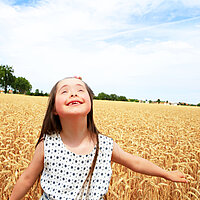 Ein fröhliches Mädchen mit Downsyndrom steht im Getreidefeld und schaut in den Himmel