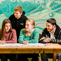 fünf Jugendliche stehen um einen Tisch und diskutieren miteinander