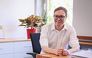 Philipp Seitz sitzt vorgebeugt an seinem Schreibtisch und lächelt