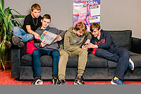 Vier Jugendliche sitzen auf der Couch und schauen sich Parteiprogramme an.