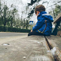 Ein Junge sitzt einsam auf einer Bank. Den Kopf gesenkt.