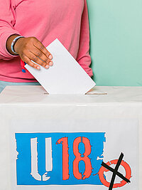 ein Stimmzettel wird in eine U18-Wahlurne geworfen.