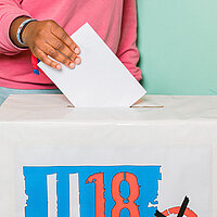 ein Stimmzettel wird in eine U18-Wahlurne geworfen.