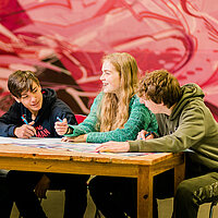 vier Jugendliche sitzen um einen Tisch und sprechen miteinander