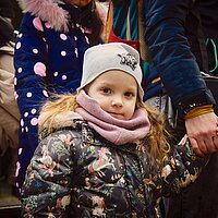 Ein Mädchen in Winterkleidung geht an der Hand und schaut in die Kamera