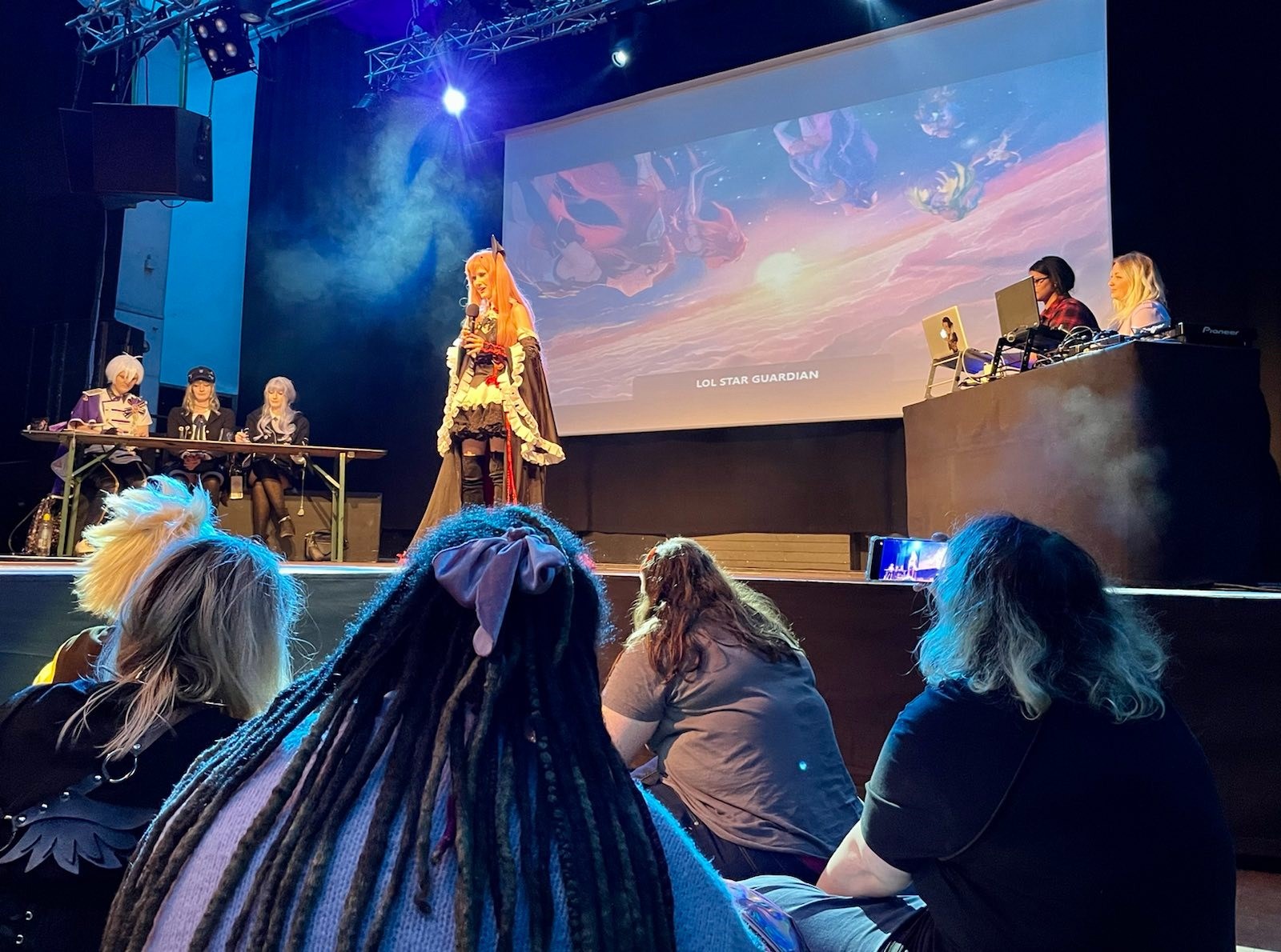  'eine Cosplayerin hält bei derPreisverleihung des Bayerischen Gamespreises eine Rede auf einer Bühne. Junge Menschen hören sitzen im Publikum. Link zu www.gamesfestival.de/